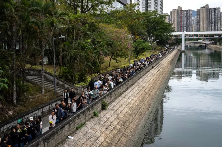 People line up to offer flowers and prayers for the victims near the site of a deadly Wednesday fire at Wang Fuk Court, a residential estate in the Tai Po district of Hong Kong's New Territories on Sunday, Nov. 30, 2025. (AP Photo/Chan Long Hei)