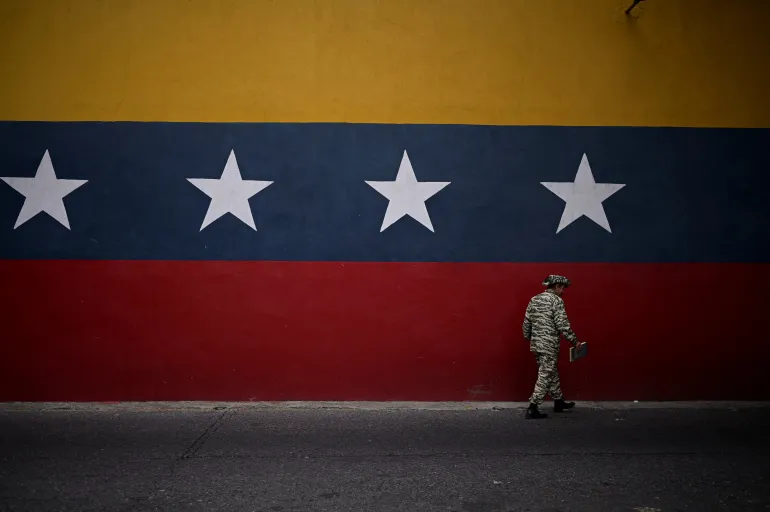 A member of the Bolivarian Militia walks past a mural with the colors of the Venezuelan flag 