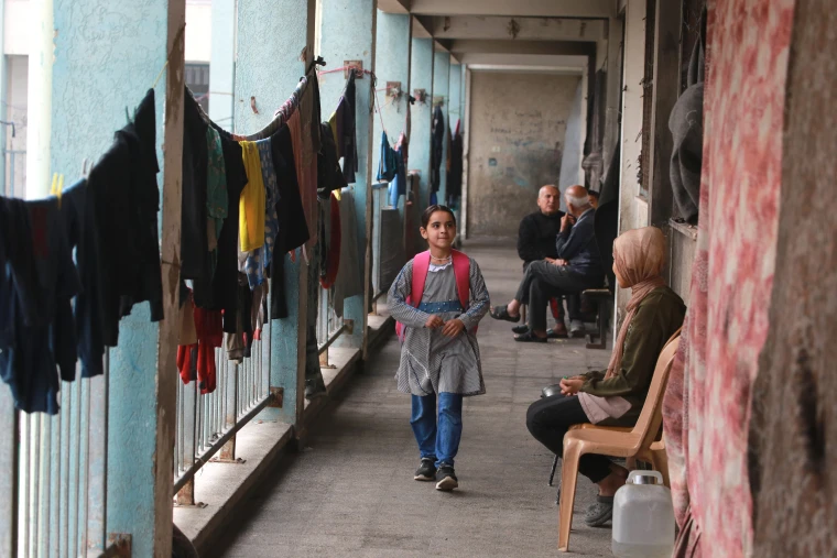 A Palestinian girl walk to a classroom, as displaced adults sit near hanging laundry at the UNRWA Deir al-Balah Joint School in the central Gaza Strip on Dec. 6.