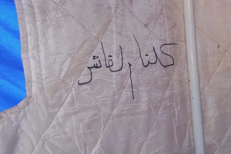 A photo of an inscription that reads "We are all el-Fasher" written in Arabic on the side of a tent