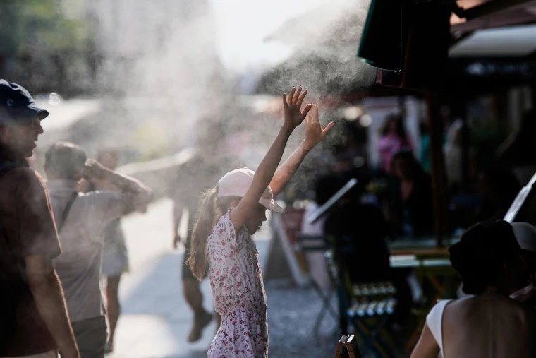 A child refreshes in front of a nebulizer outside, water is sprayed from above into mist