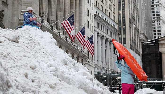 Children sled and play on a snow pile outside the New York Stock Exchange (NYSE), after a major winter storm spreads across a large swath of US, in New York City, on January 26, 2026. — Reuters