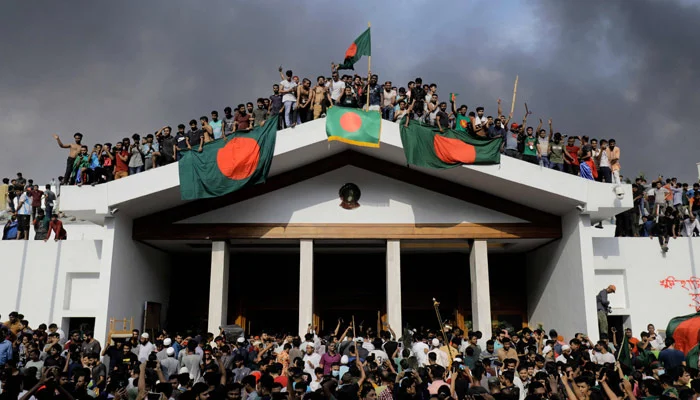 Anti-government protestors display Bangladeshs national flag as they storm Prime Minister Sheikh Hasinas palace in Dhaka on August 5, 2024. — AFP