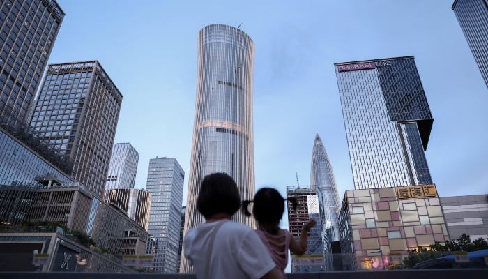 A woman holds a child near office buildings in Shenzhen, Guangdong province, China, September 15, 2025. — Reuters