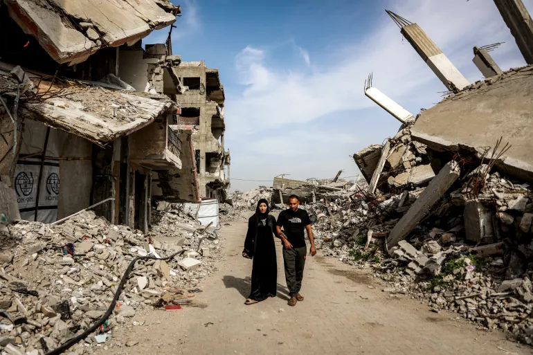 Etedal Rayyan (29), who recently returned back to Gaza from Egypt through the Rafah border crossing, walks with and her husband past the rubble of destroyed buildings in the Jabalia camp for Palestinian refugees in the northern Gaza Strip on February 8, 2026.