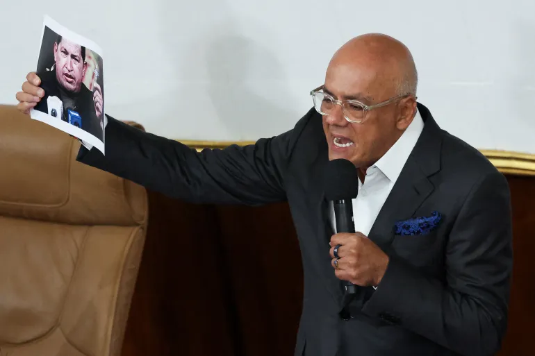 Jorge Rodriguez speaks into a microphone and holds up a picture of Nicolas Maduro