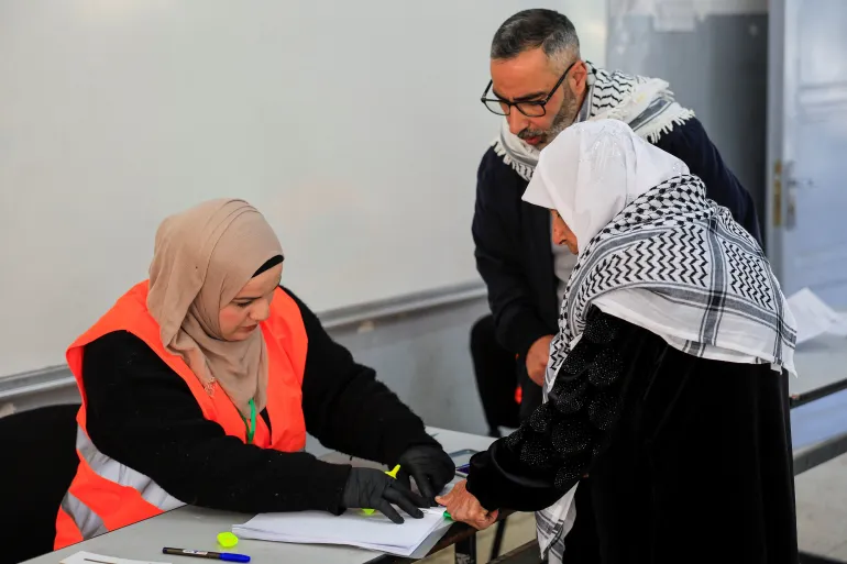 A polling official assists a Palestinian woman as she votes during the municipal council election, in Hebron, in the Israeli-occupied West Bank, April 25, 2026. REUTERS/Mussa Qawasma