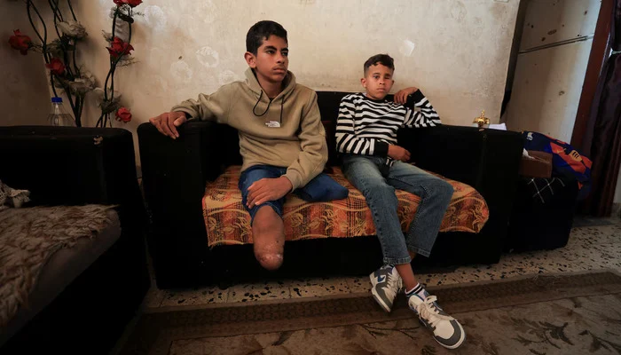 Fadel Al-Naji, 14, who lost both legs, sits beside his brother Amir Al-Naji, 11, who lost an eye, after they were injured in an Israeli strike, at their home in Gaza City, April 10, 2026.