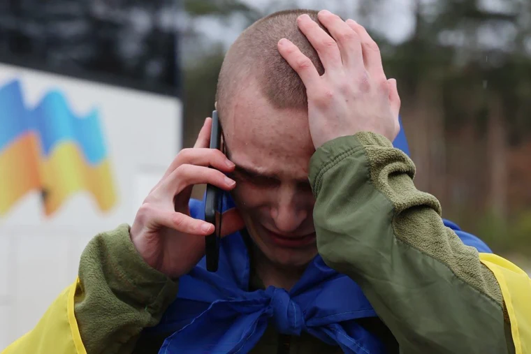 A former Ukrainian prisoner of war (POW), wrapped with a Ukrainian national flag, speaks on a mobile phone following an exchange at an undisclosed location on April 11.