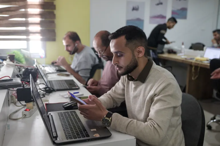 Man at desk working on a computer, others in the background