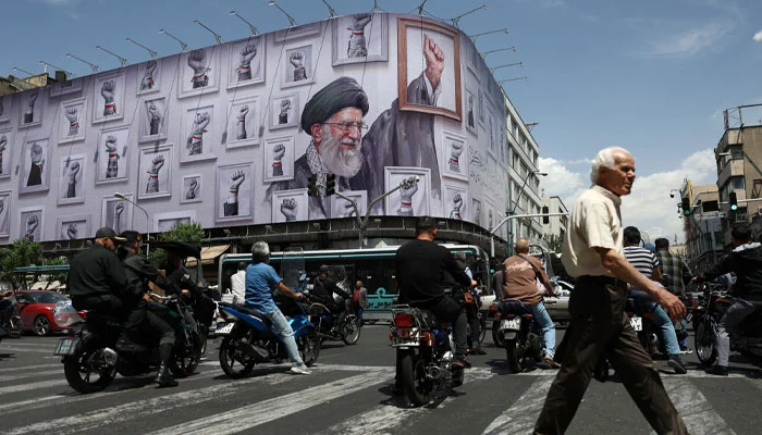People ride motorcycles near a billboard featuring an image of the late Supreme Leader of Iran, Ayatollah Ali Khamenei, in Tehran, Iran, May 6, 2026.