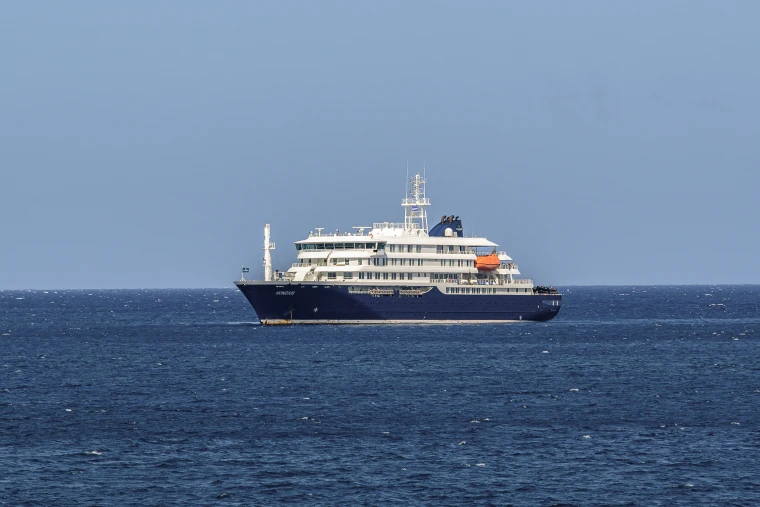 A blue and white cruise ship floats in calm waters under a clear blue sky.