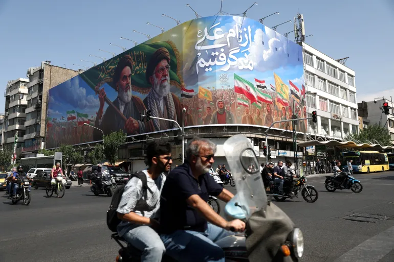 People ride past a billboard depicting the late leader of the Islamic Revolution, Ayatollah Ruhollah Khomeini, and the late Iran's Supreme Leader Ayatollah Ali Khamenei,