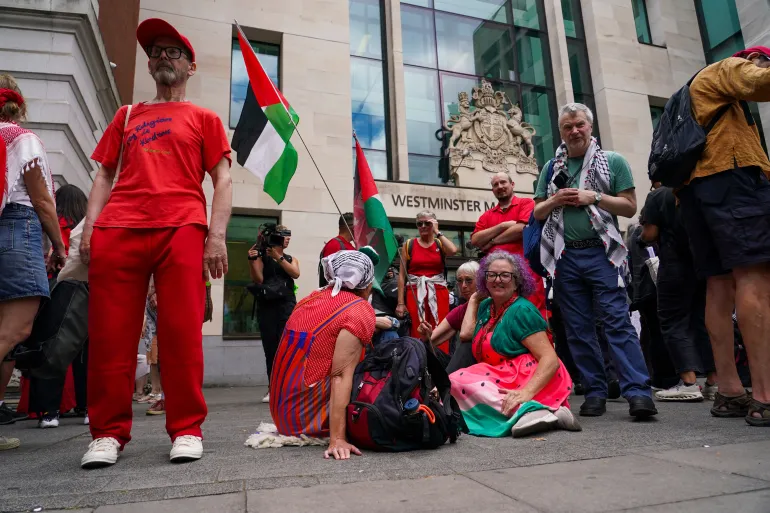 Demonstrators sit outside the Westminster Magistrates Court in London on Thursday as a plea hearing for 25 people accused of showing support for Palestine Action takes place