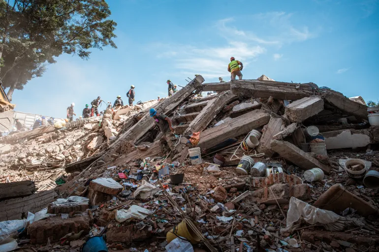 Firefighters and volunteer rescuers climb what remains of the Vanessa apartment building in Cali, Colombia. After a week of searching, the wreckage no longer yields any sign of sur- vivors. [Euan Wallace / Al Jazeera]
