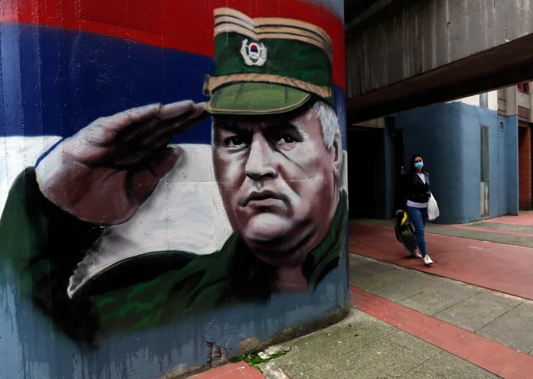 A woman wearing a face mask walks past graffiti depicting former Bosnian Serb wartime general Ratko Mladic in Belgrade, Serbia, Thursday, Nov. 12, 2020. Mladic was convicted by a UN war crimes tribunal in 2017 and sentenced to life imprisonment for masterminding crimes by Bosnian Serb forces throughout the war that left 100,000 dead. (AP Photo/Darko Vojinovic)