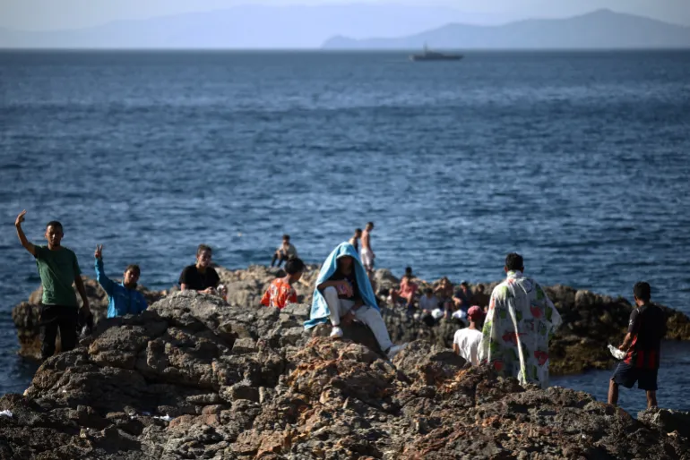 A group of migrants wave from the coastal rocks with a Guardia Civil patrol boat visible in the background, near the border post of the Spanish enclave of Ceuta on August 2