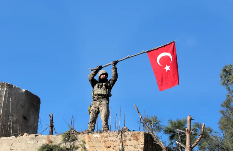 FILE -- In this Sunday, Jan. 28, 2018 file photo, a soldier waves a Turkish flag as Turkish troops secure Bursayah hill, which separates the Kurdish-held enclave of Afrin from the Turkey-controlled town of Azaz, Syria. The planned U.S. troop withdrawal opens a void in the north and east of Syria, and the conflicts and rivalries among all the powers in the Middle East are converging to fill it. (AP Photo, File)