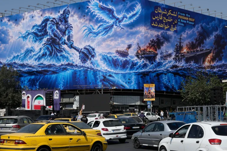 Vehicles drive past a billboard depicting a Persian legendary hero and flying figure hitting US aircraft carriers alongside a message in English: ‘From the Persian Gulf a new power rises’, and in Farsi, ‘The army of Satan will be drowned in the Persian Gulf’, at Islamic Revolution Square in downtown Tehran, Iran, Monday, September 14, 2026
