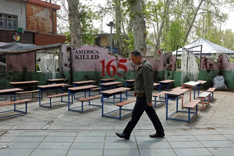 A man walks past a memorial depicting a symbolic classroom representing the Minab school children is displayed in a square in Tehran on May 3, 2026. Iran on April 28 shared a breakdown of the death toll from the deadly strike on the school on the first day of the Middle East war. Seventy-three boys and 47 girls were killed in the February 28 strike in Minab, state broadcaster IRIB and local media reported. The attack happened on the day the United States and Israel launched attacks across Iran. In retaliation, Tehran struck targets in Israel and Gulf nations. (Photo by AFP) /