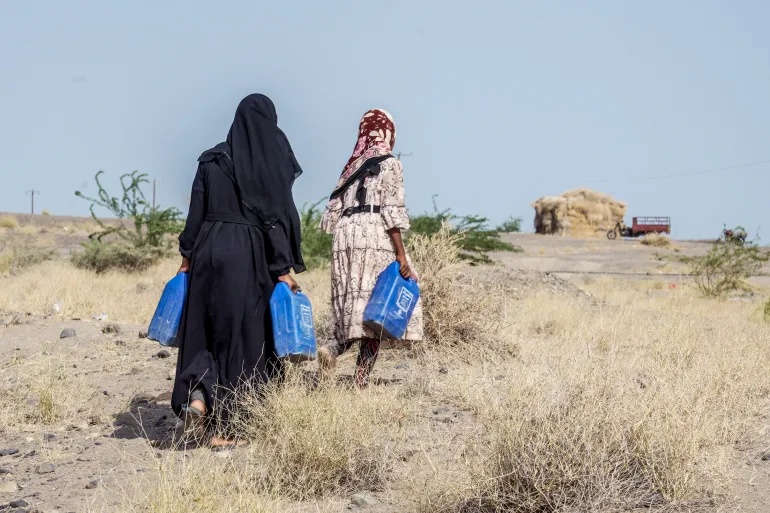 Internally displaced (IDP) Yemeni women who fled their homes with their families due to renewed clashes between Yemen's Saudi-backed government forces and the country's Houthi rebels, carry jerrycans after seeking shelter in Mocha, on the Red Sea coast of Yemen on September 7, 2026. [AFP]